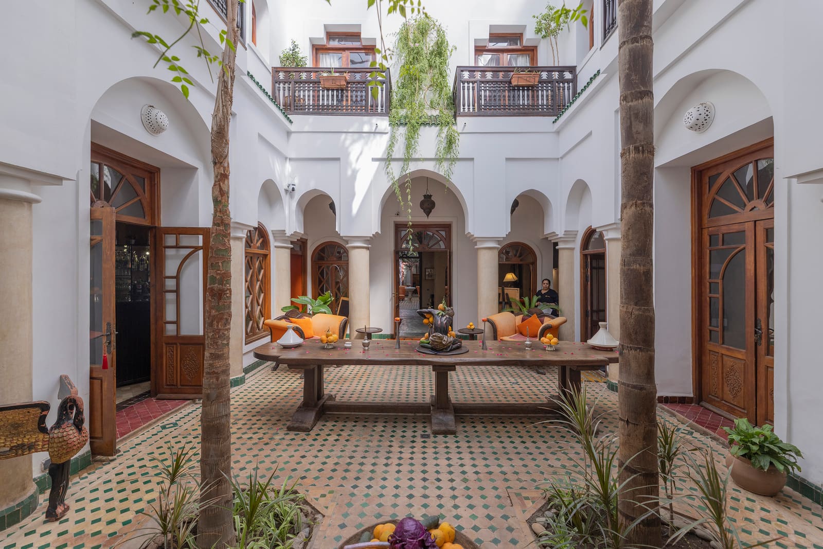 Le grand patio du riad : table sous l'olivier, palmiers et arcades de chaux blanche